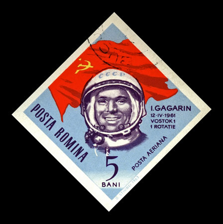 ROMANIA - CIRCA 1964: canceled stamp printed in Romania shows soviet astronaut Yuri Gagarin, 1st man in the space, red soviet flag, circa 1964. vintage postal stamp isolated on black background.のeditorial素材