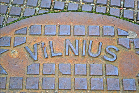 focus on text. Vilnius city text message on vintage damaged metal manhole surface closeup, retro technology diversityの写真素材