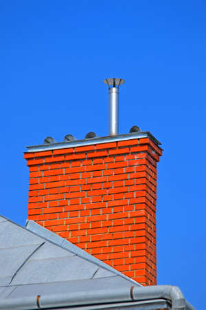 orange chimney brick pipe on the roof on blue sky in sunny day, modern construction, environment pollution diversityの写真素材