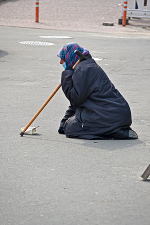 unknown elderly grandmother with striped headscarf and stick in black suit sitting on her knees hunched over and asking for help on March 29, 2021 in Kiev, Ukraine.のeditorial素材