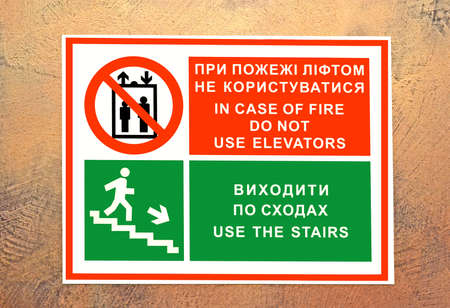 in case of fire do not use elevators, use the stairs - emergency exit sign. warning message on ukrainian language on signboard on the vintage stone textured wall,
modern securityの写真素材