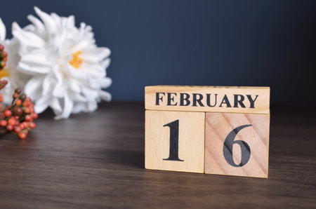 February 16, Date cover design with calendar cube and white Paeonia flower on wooden table and blue background.の写真素材