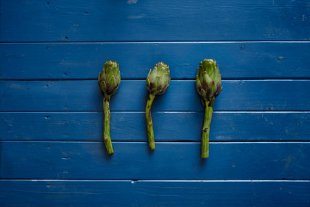 three fresh artichokes on blue wooden tableの写真素材