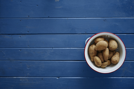 potatoes in a white sieve on blue tableの写真素材