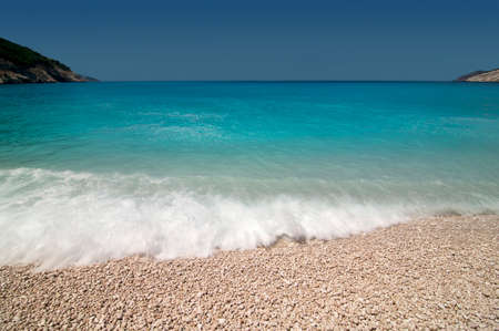 Shore break on beach with turquoise blue water and small stones.の写真素材