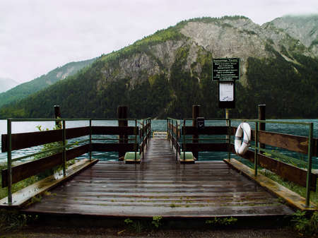 A small pier on the shore of the Grosser-Alpsee lake in cloudy weather. Closed entrance to the pier after a rainの写真素材