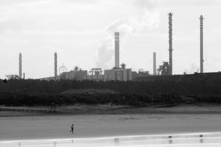 man running by the beach in front of the chimneys of one trains in black and whiteの写真素材