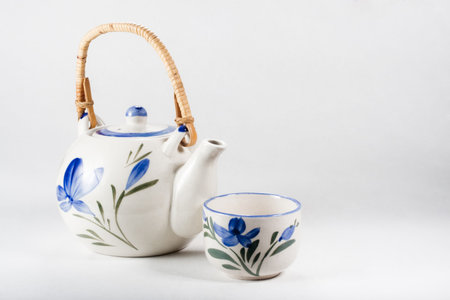 Tea-pot and cup of white porcelain refined decorated with floral motives in blue and green on white backgroundの写真素材