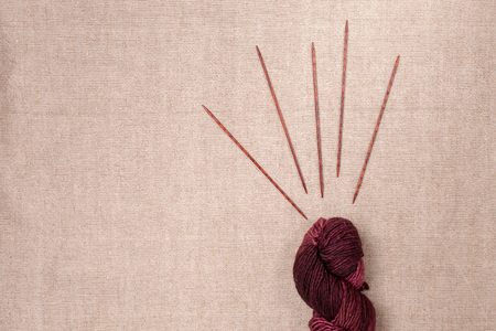 Wine-colored yarn with wooden knitting needles on canvas background with space for textの写真素材