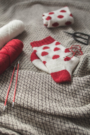 White knitted socks with red dots, handmade socks with socks yarn on blanket background