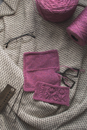 Yarn with scissor, knitting size ruler and glasses on vintage blanket background.