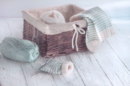 Skeins in basket and sock. Azure wool yarn and striped knitting handmade sock on needles.
