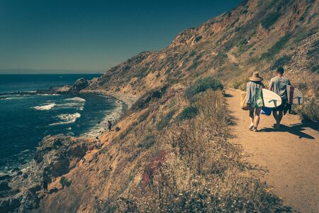 Young couple walking on a rugged trail with their surfboards in Palos Verdes Estates, Californiaの写真素材