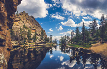 Perfectly still water on Gem Lake with reflection of blue sky, clouds, mountains, and trees, Estes Park, Coloradoの写真素材