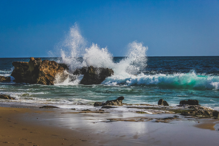 Beautiful beachfront view of waves crashing into rock formations on a sunny day with stunning blue water, Laguna Beach, Californiaの写真素材