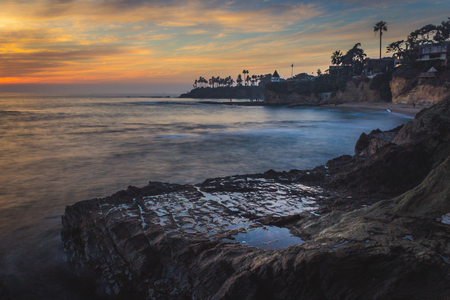 Beautiful coastal view of a colorful sky at sunset with stunning blue water, waves crashing into rock formations, and water from tide pools reflecting the sky, Diverâs Cove, Laguna Beach, Californiaの写真素材