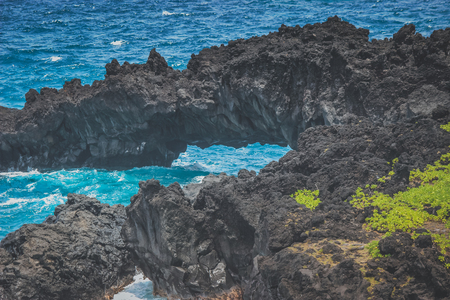 Beautiful black rock arches at Waianapanapa Black Sand Beach with vibrant blue water near the Road to Hana, Maui, Hawaiiの写真素材