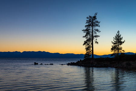 Clear sky at sunset at Sand Harbor with calm water, silhouettes of trees, and mountains in the background, Lake Tahoe, Carson City, Nevadaの写真素材