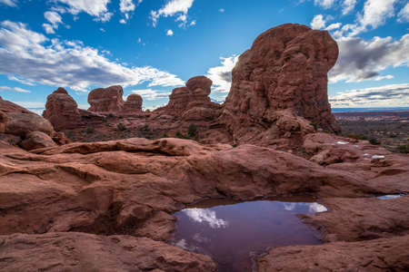 Gorgeous view atop of Turret Arch surrounded by tall sandstone spires and puddles of water that reflect the cloudy blue sky, Arches National Park, Moab, Utahの写真素材