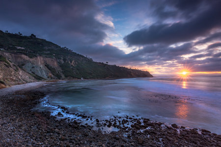 Embark on a serene journey along Bluff Trail, Palos Verdes, Estate, where the sun dips below Bluff Cove, illuminating rugged cliffs and serene ocean waves, creating a tranquil coastal landscape.の写真素材