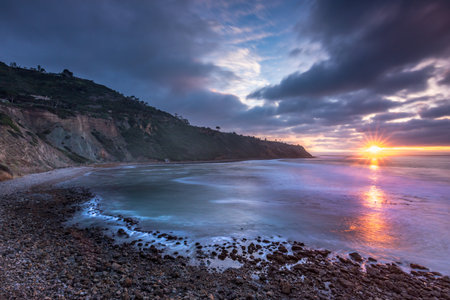 Embark on a serene journey along Bluff Trail, Palos Verdes, Estate, where the sun dips below Bluff Cove, illuminating rugged cliffs and serene ocean waves, creating a tranquil coastal landscape.の写真素材