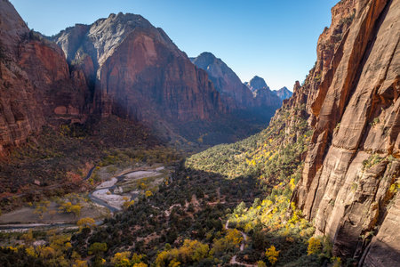 Majestic sandstone cliffs tower over the Virgin River, surrounded by vibrant autumn foliage, inviting relaxation and exploration in Springdale, Utah.の写真素材
