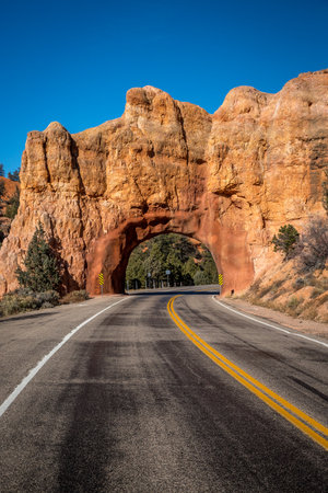 Discover the scenic beauty of Panguitch, Utah, where a winding road passes through a stunning sandstone arch surrounded by nature.の写真素材