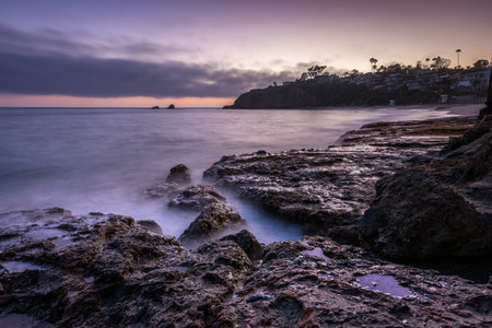 Waves gently crash on rocky shores as the sun sets over Crescent Bay Beach in Laguna Beach,...