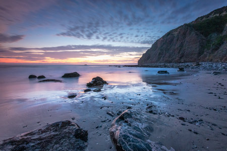 Waves gently lap against the rocky shore as the sun sets behind the cliffs at Dana Cove in Southern California, creating a serene atmosphere.の写真素材