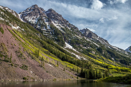 Snow-capped peaks tower above vibrant green slopes near Maroon Lake. Colorado's Pyramid Peak creates a stunning backdrop for nature lovers.の写真素材