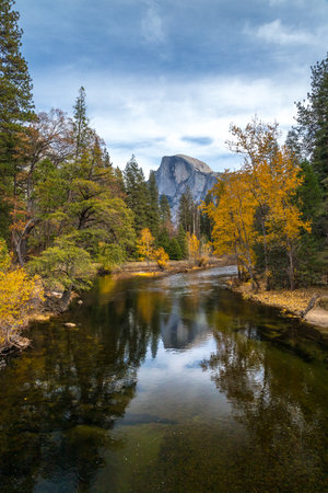 Autumn colors reflect in calm waters as Half Dome rises in the distance, creating a peaceful and scenic landscape in Yosemite National Park.の写真素材
