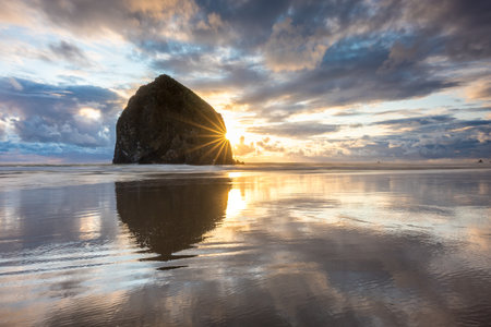 Breathtaking sunset at Haystack Rock on Cannon Beach with colorful sky and reflections from the calm water on the beachの写真素材