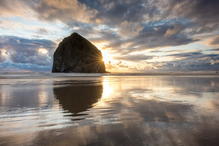 Breathtaking sunset at Haystack Rock on Cannon Beach with colorful sky and reflections from the calm water on the beachの写真素材