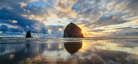 Breathtaking sunset at Haystack Rock on Cannon Beach with colorful sky and reflections from the calm...