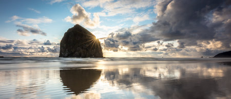 Breathtaking sunset at Haystack Rock on Cannon Beach with colorful sky and reflections from the calm water on the beachの写真素材