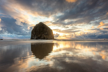 Breathtaking sunset at Haystack Rock on Cannon Beach with colorful sky and reflections from the calm water on the beachの写真素材