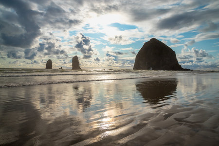 Breathtaking sunset at Haystack Rock on Cannon Beach with colorful sky and reflections from the calm water on the beachの写真素材