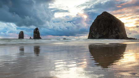 Breathtaking sunset at Haystack Rock on Cannon Beach with colorful sky and reflections from the calm...