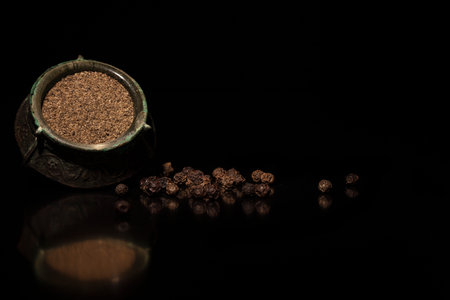 Powdered black pepper and pepper corns on black