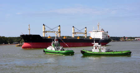 Port tugboat meets a large cargo ship.の写真素材