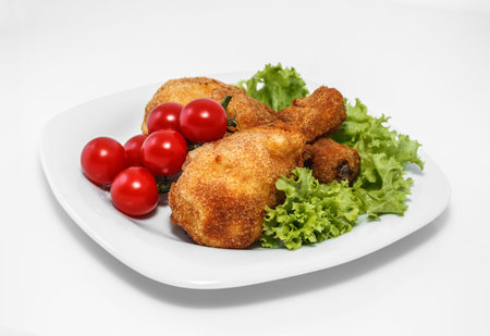 Fried chicken pieces on a plate with lettuce and tomatoes. Taken on a sheet of white plastic. Is not an isolate.の写真素材