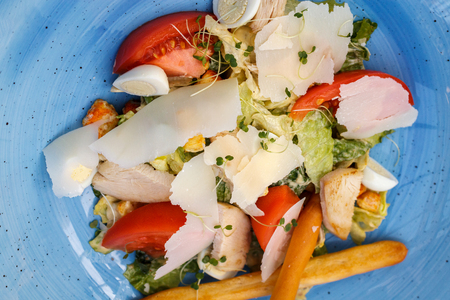 Fresh salad of chicken with vegetables and cheese, on a blue backgroundの写真素材