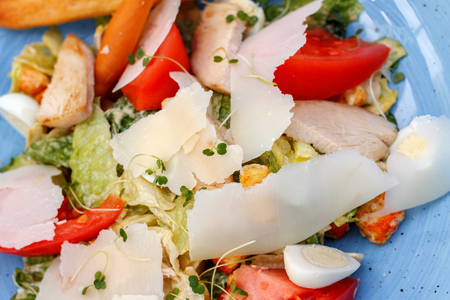 Fresh salad of chicken with vegetables and cheese, on a blue backgroundの写真素材