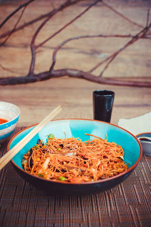 Asian noodles with soy sauce and shiitake mushrooms served in ceramic bowl on blue burlap cloth. Wooden table background with tree decorative branchの写真素材