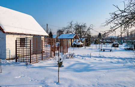 Snowy Winter Garden with Bench and Small Houses at Sunriseの写真素材