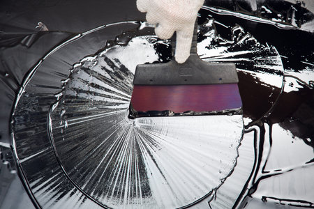Builder's hand with a spatula and bitumen draws a circle