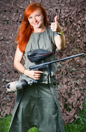 A girl holds a paintball gun and motioned showing thumbs upの写真素材