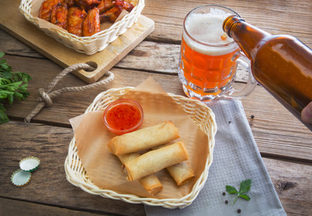 Still life with a bottle of beer and stuffed pancakes and chicken wings on an old wooden table