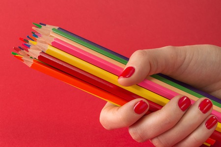 womans hand holding colored pencils on red backgroundの写真素材