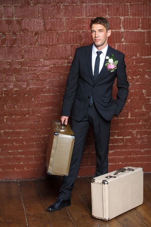 groom is a brick wall with two suitcasesの写真素材